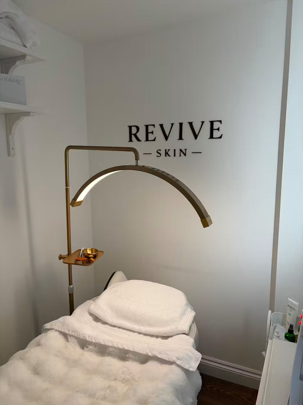 Sala trattamenti per la cura della pelle con l'insegna personalizzata "REVIVE SKIN" dorata appesa alla parete.